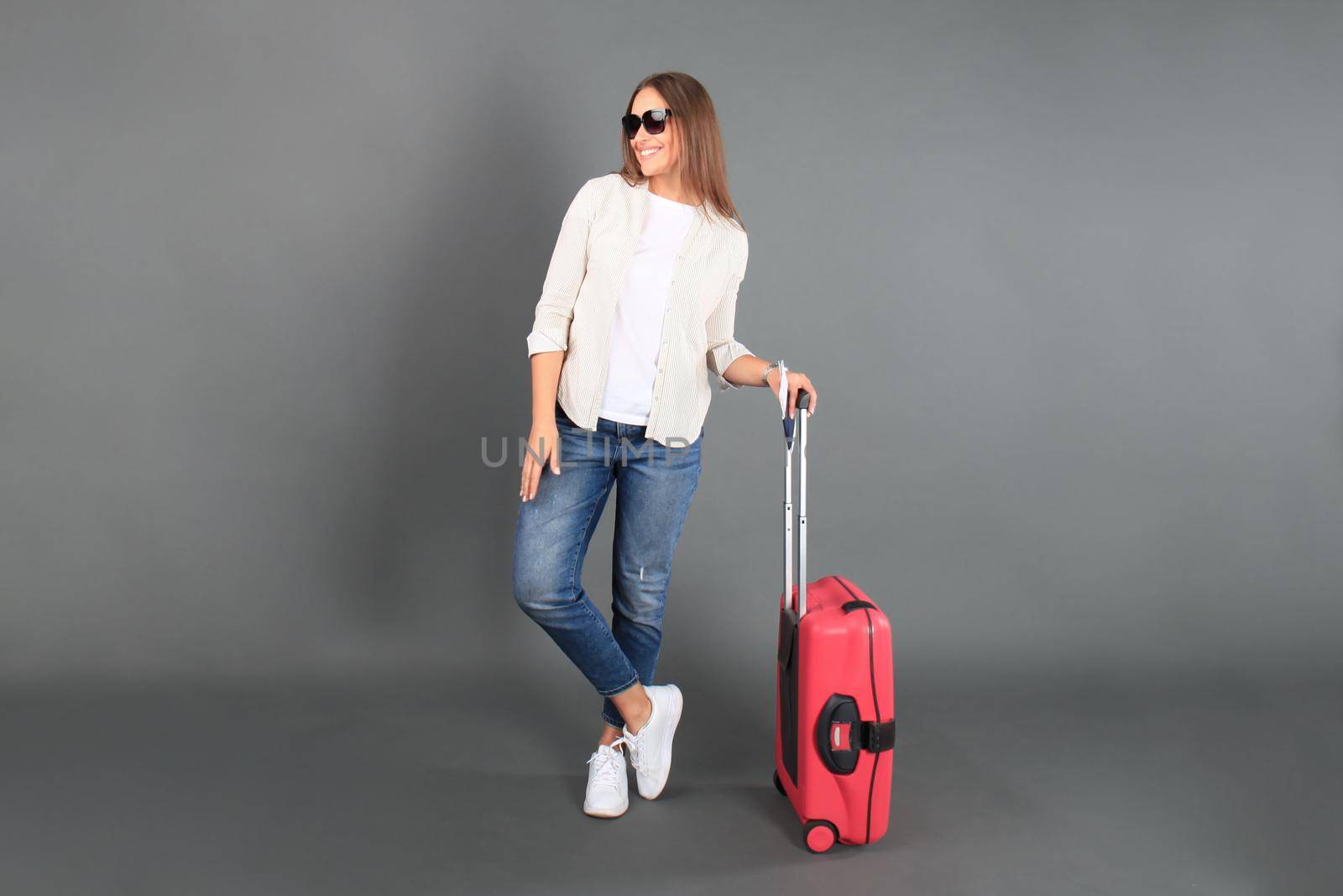 Young tourist girl in summer casual clothes, with sunglasses, red suitcase, passport, tickets isolated grey background.