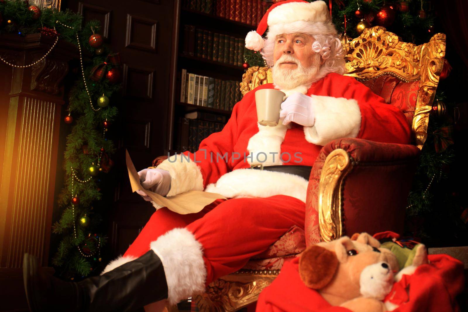 Santa Claus having a rest in a comfortable chair near the fireplace at home. by tsyhun