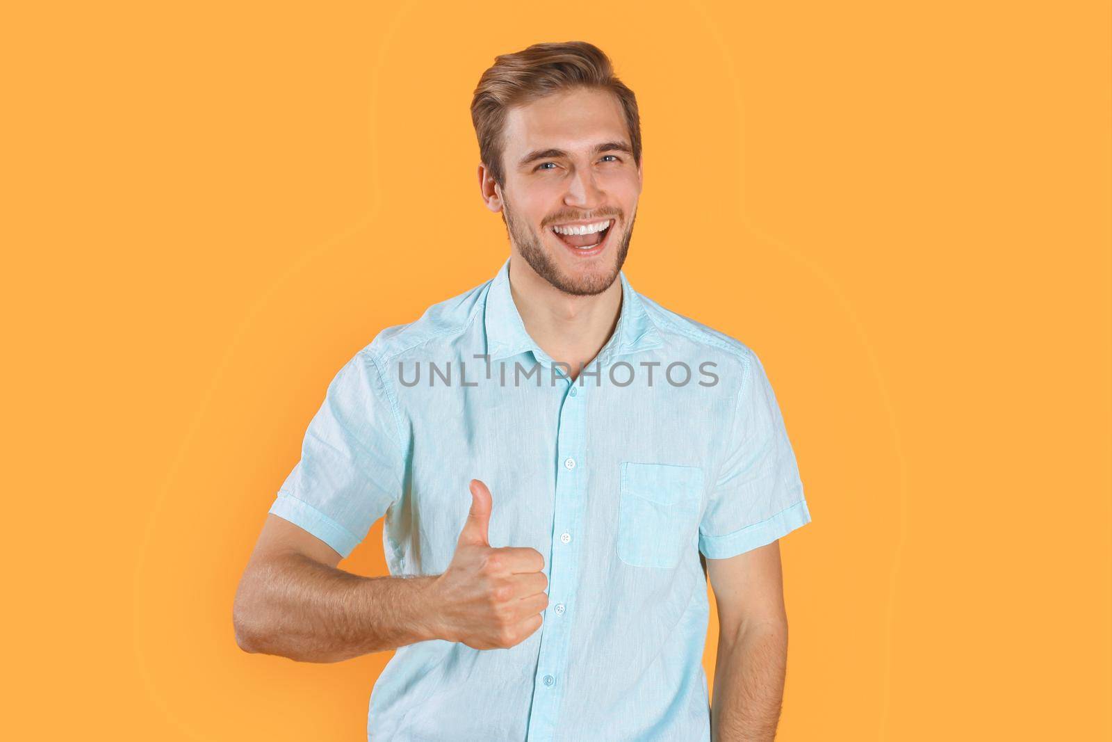 Young man showing thumbs up isolated over yellow background by tsyhun