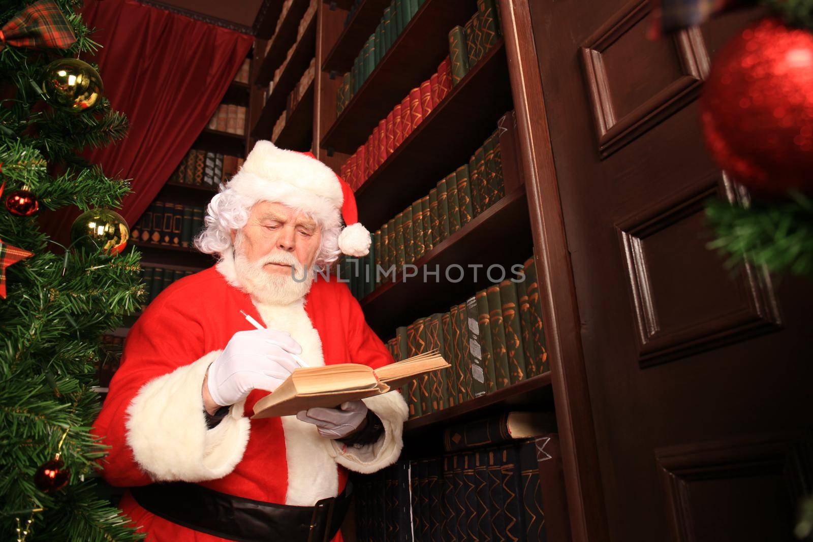 Santa standing at the Christmas tree and reading a book.