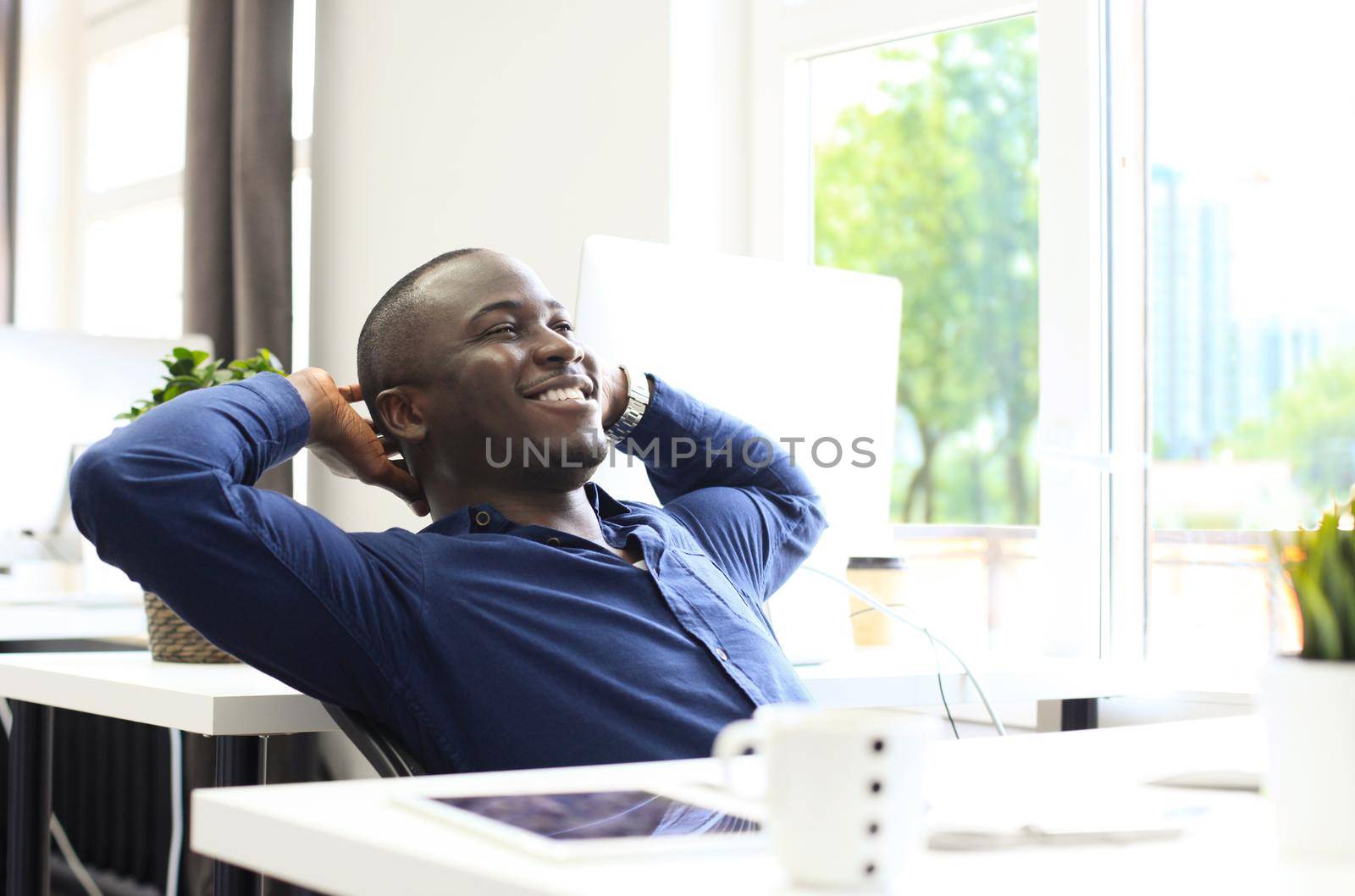 Relaxed Afro American business man sitting at his desk looking into the air by tsyhun