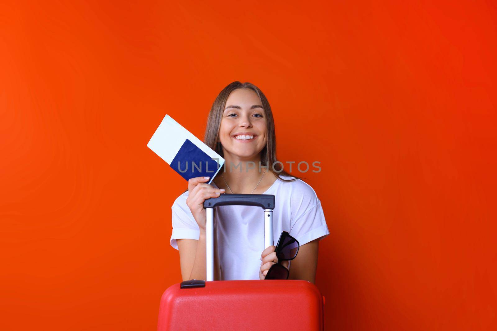 Young tourist girl in summer casual clothes, with sunglasses, red suitcase, passport isolated on red background.