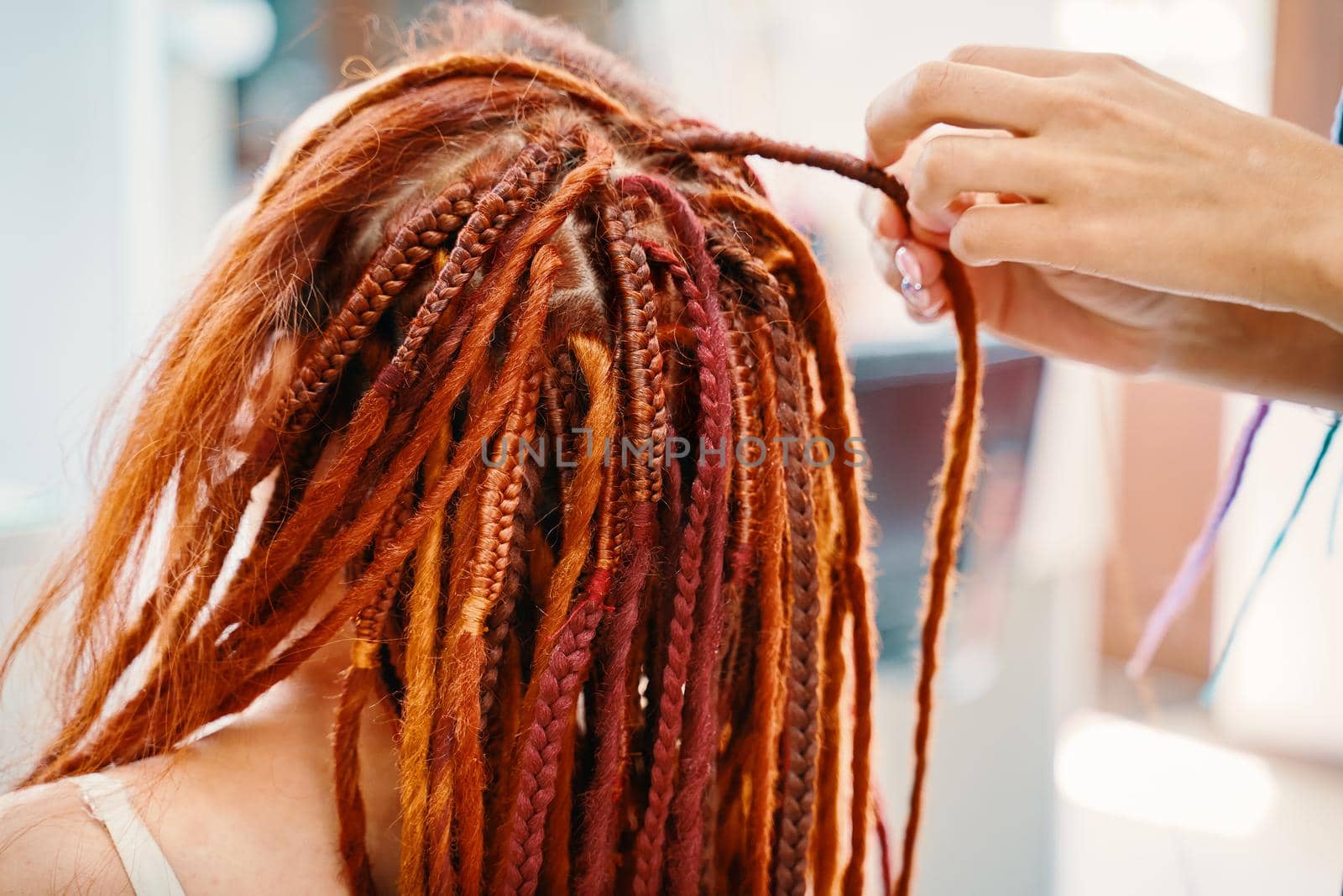 Woman hairdresser weaves girl ginger dreadlocks. Stylish therapy professional care concept. Close up of braiding process plait with colored kanekalon. Hippie style hairstyle. Beauty salon services.