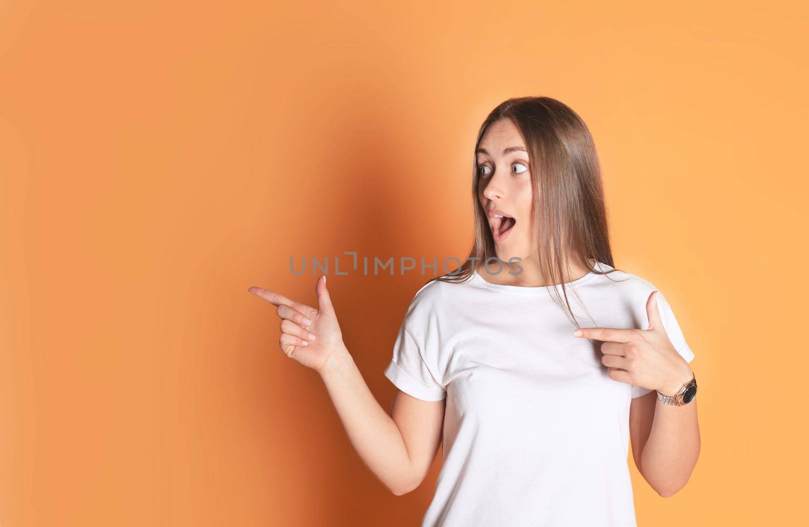 Young woman in basic clothing smiling and pointing finger at copyspace isolated on yellow background. by tsyhun