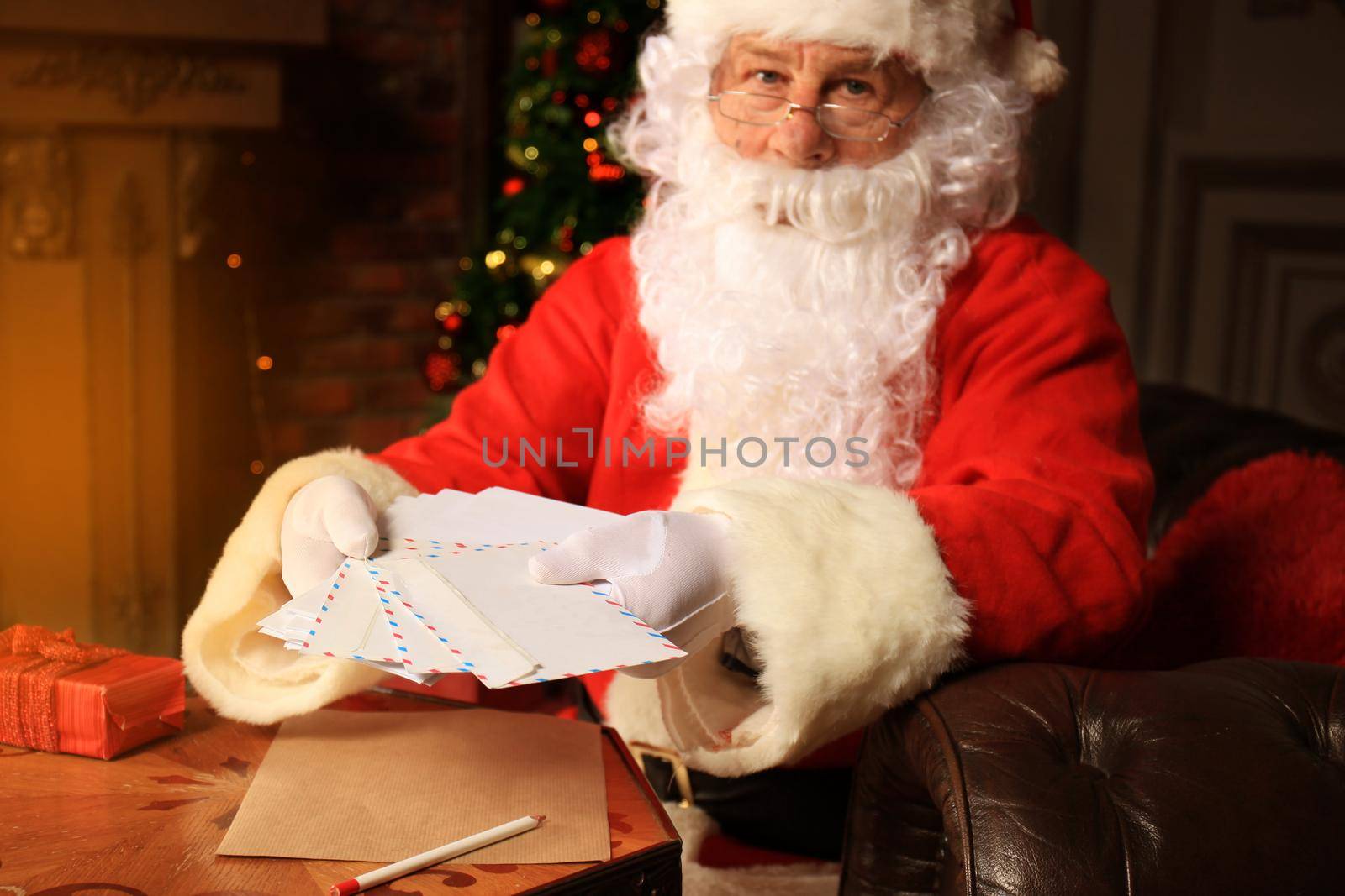 Santa sitting at the Christmas tree, holding Christmas letters and having a rest by the fireplace.