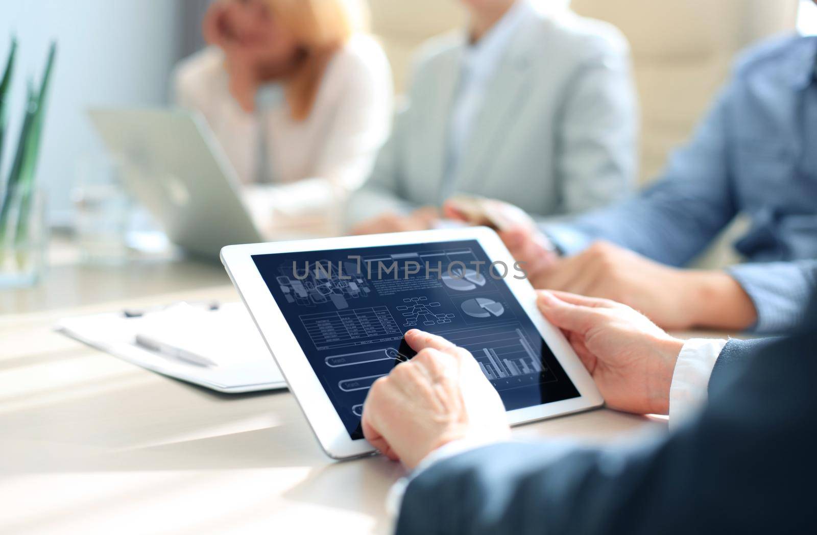 business documents on office table with smart phone and laptop computer and graph business with social network diagram and three colleagues discussing data in the background