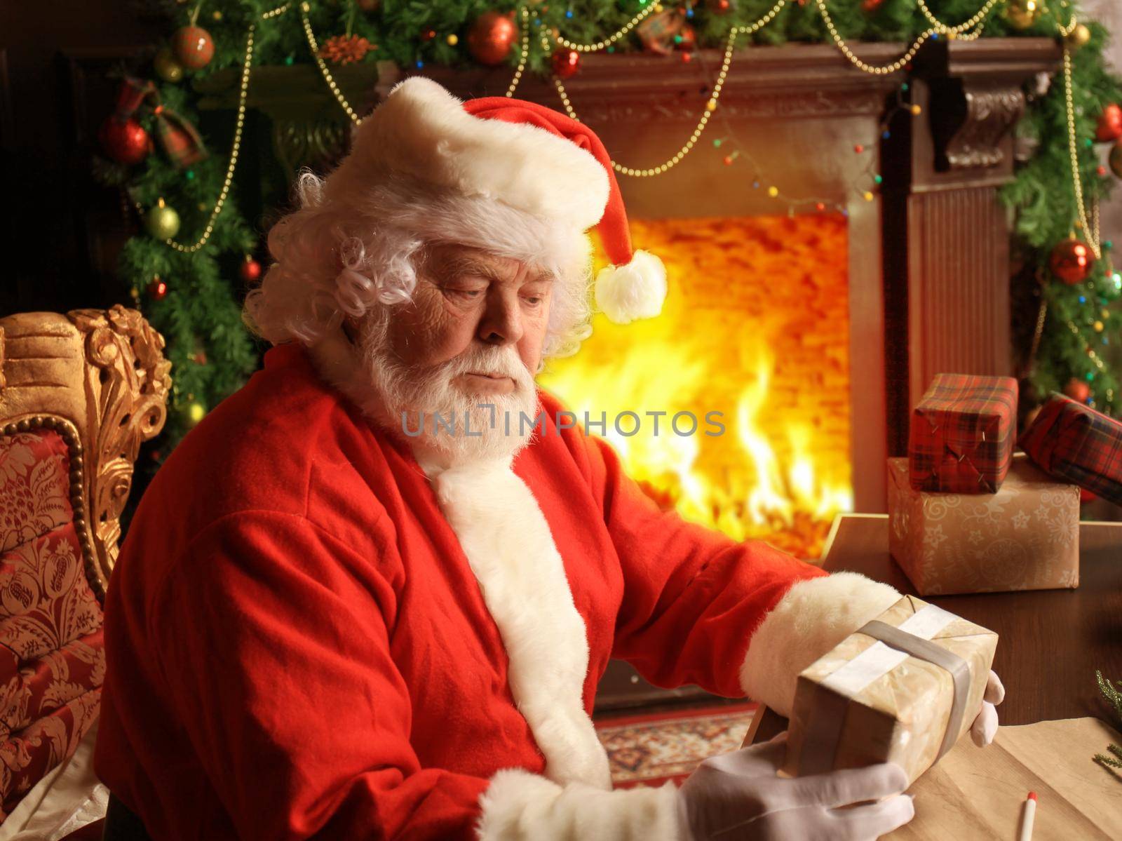 Portrait of happy Santa Claus sitting at his room at home near Christmas tree with gift box. by tsyhun