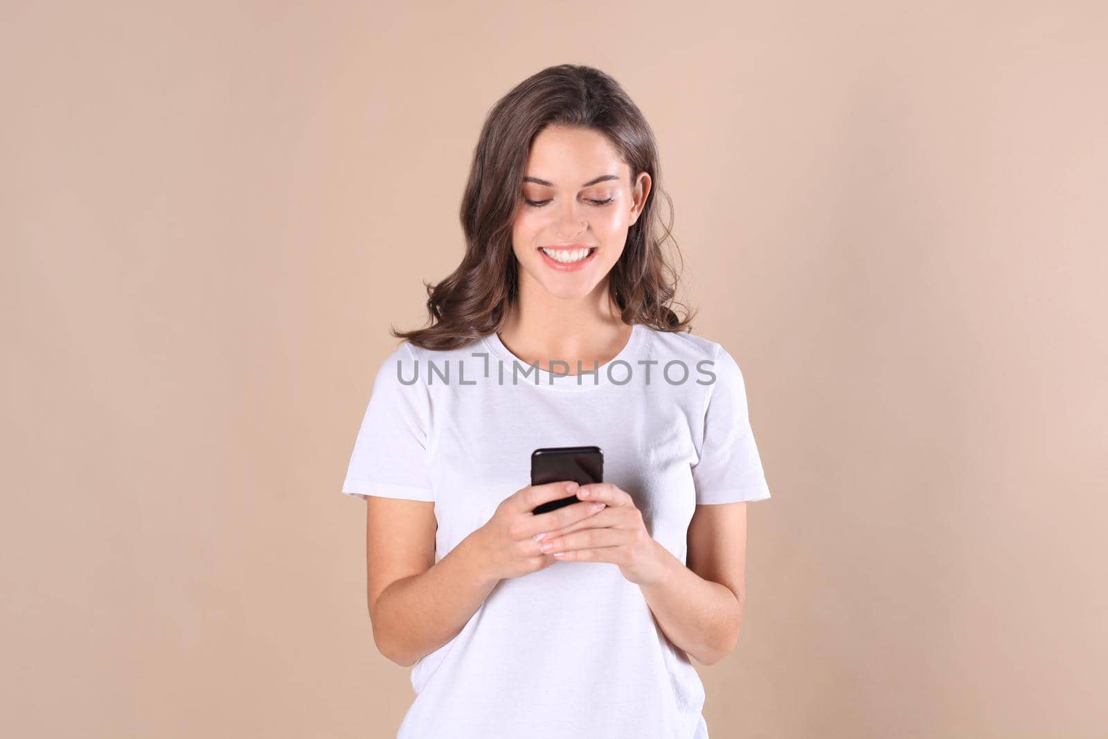 Young woman dressed in basic clothing isolated on beige background, using mobile phone