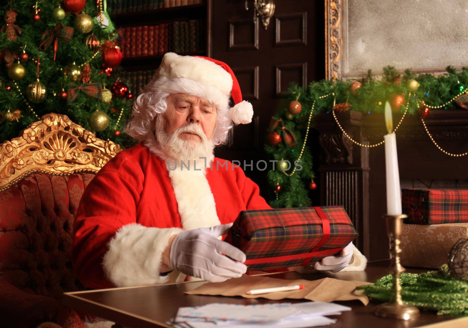 Portrait of happy Santa Claus sitting at his room at home near Christmas tree with gift box. by tsyhun