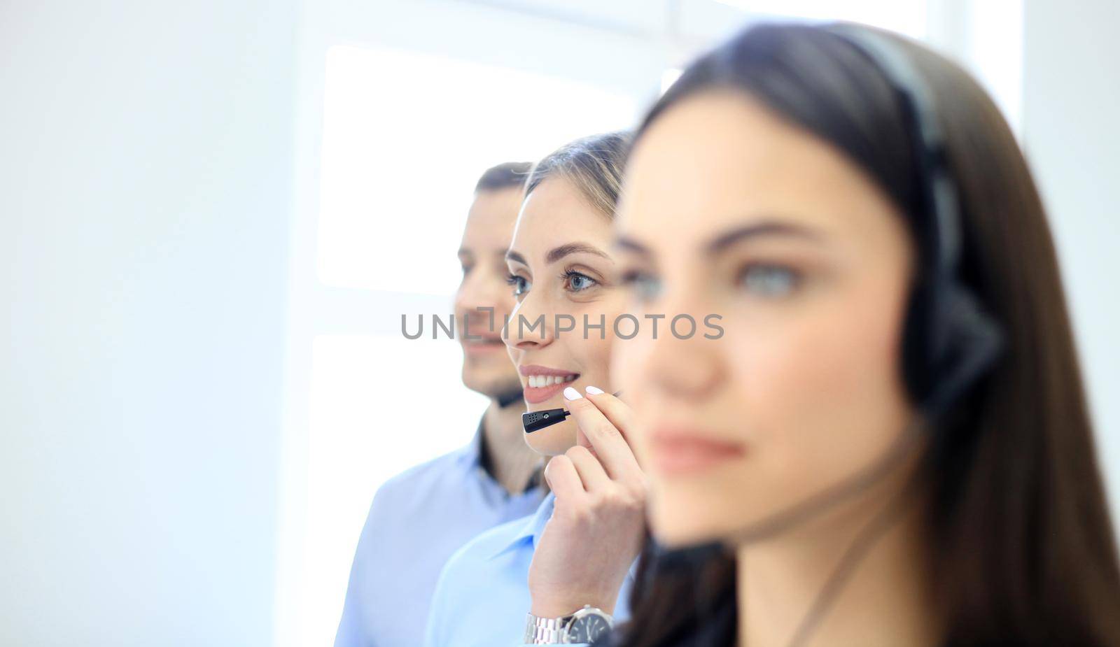 Portrait of call center worker accompanied by her team. Smiling customer support operator at work.