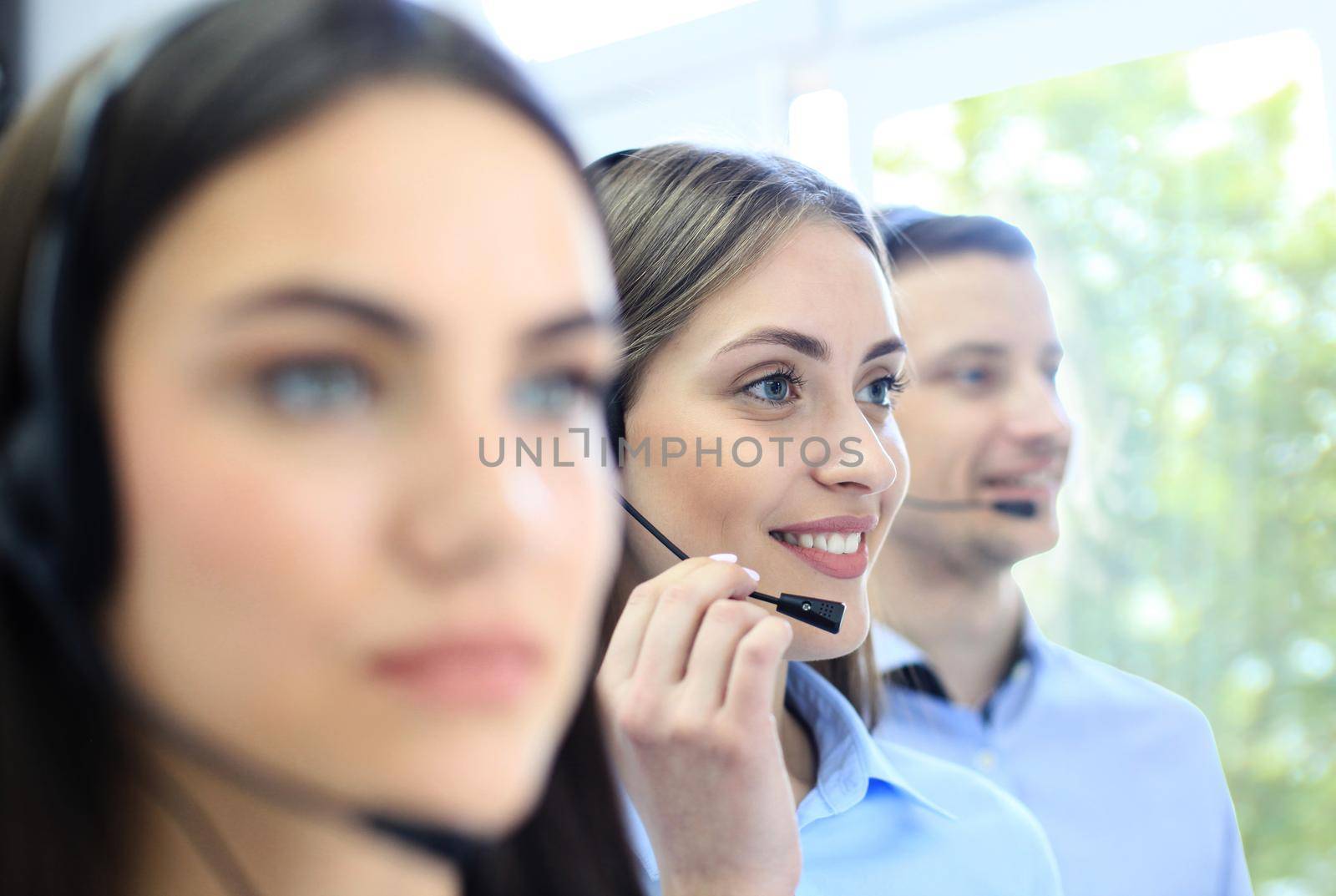 Portrait of call center worker accompanied by her team. Smiling customer support operator at work.