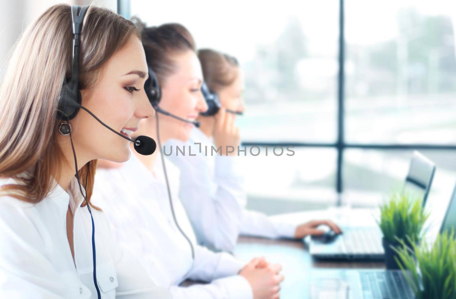 Portrait of smiling female customer service agent wearing headset with colleagues working in background at office. by tsyhun