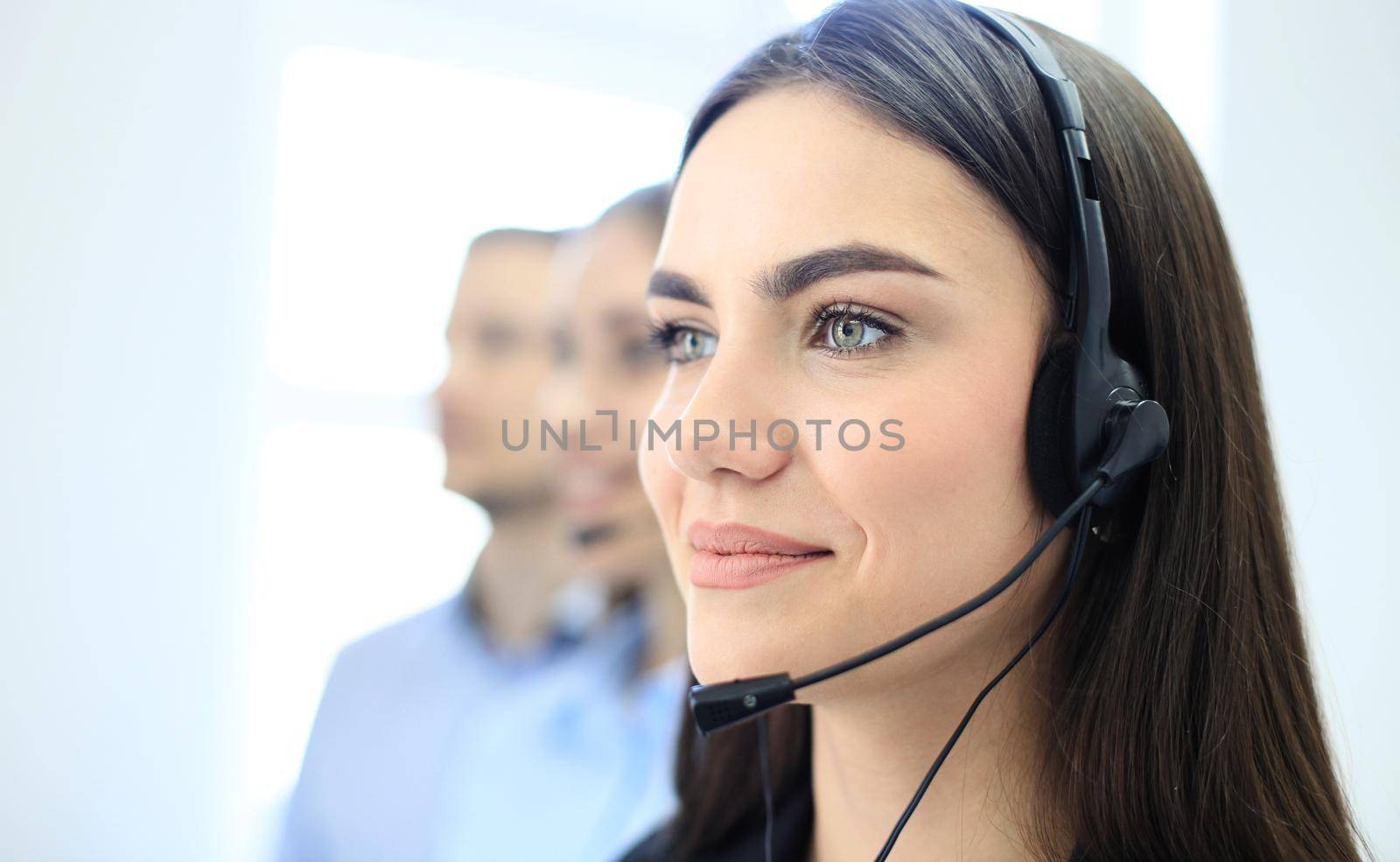 Smiling female call centre operator doing her job with a headset while looking at camera