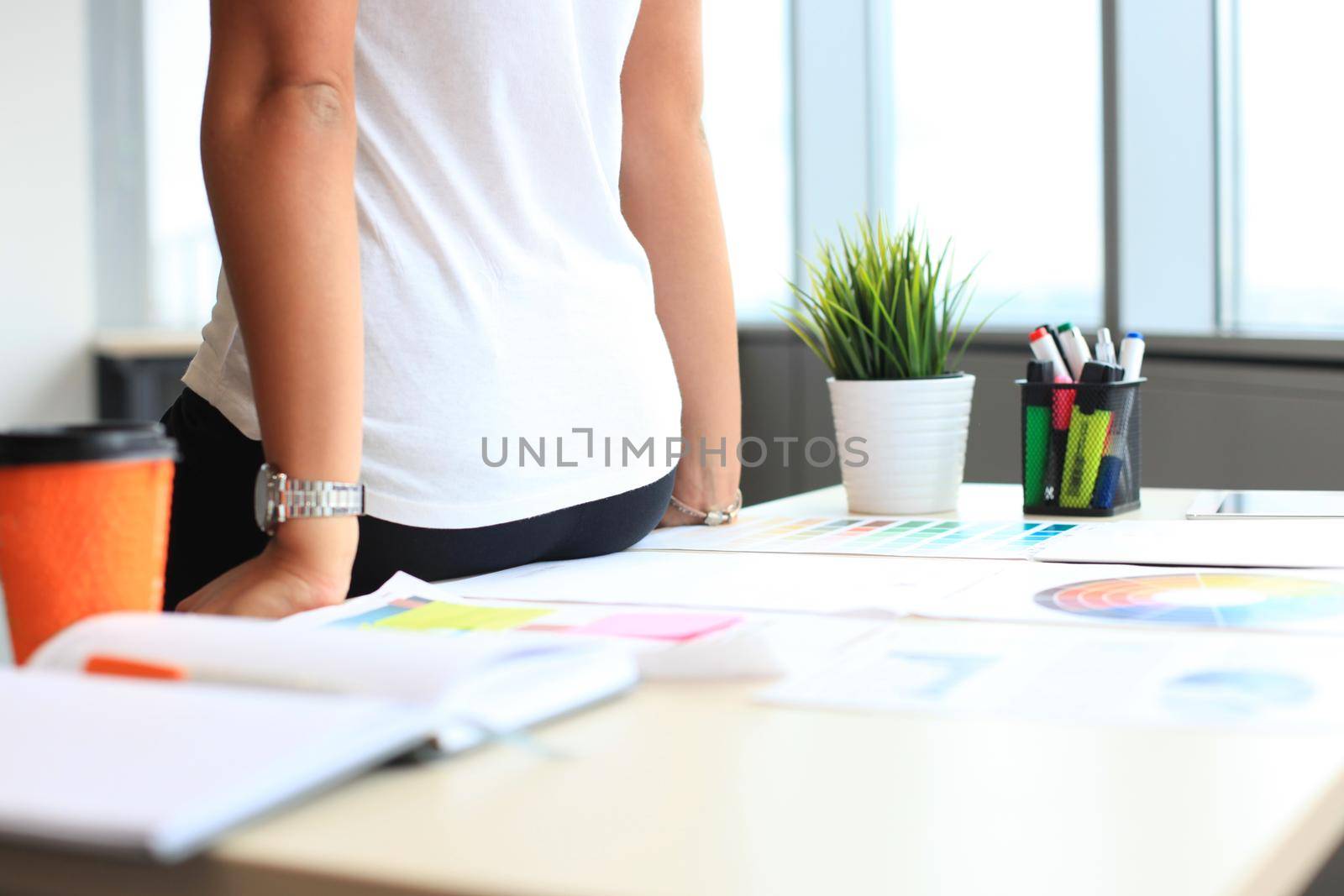 Young woman standing near desk with instruments, plan and laptop by tsyhun