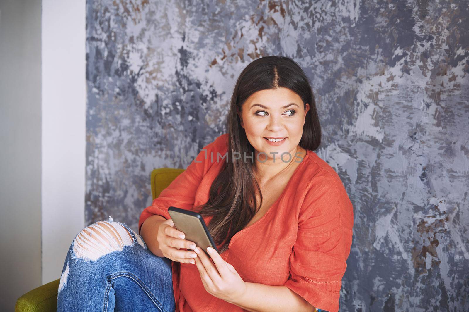 Plus size model sitting on the chair and using smartphone