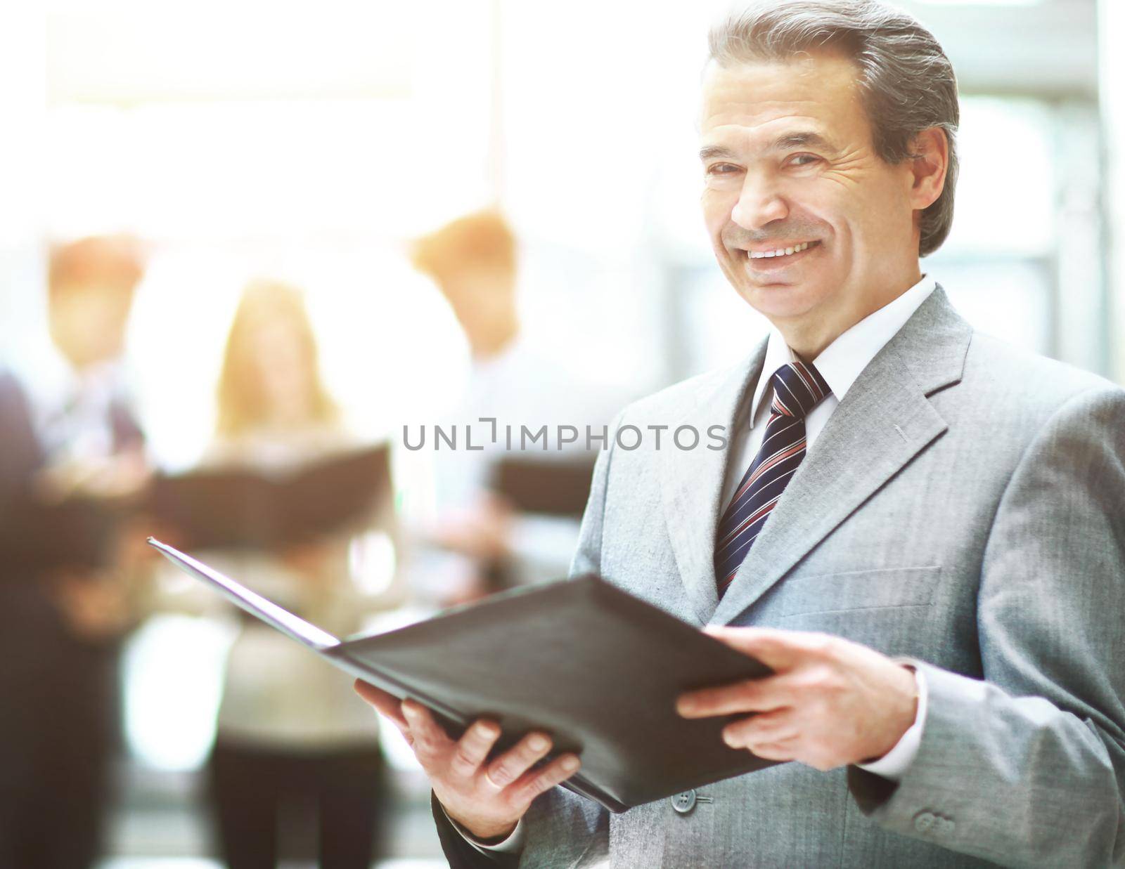 business man standing with his staff in background at office by SmartPhotoLab