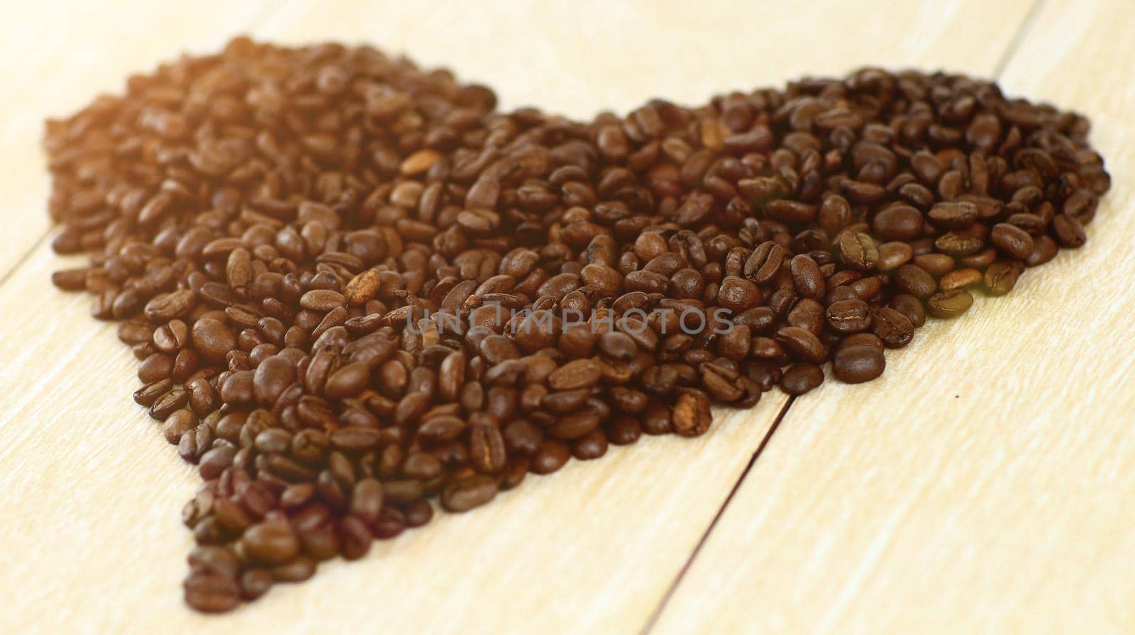 close up.black coffee beans folded in the shape of a heart on a wooden table.