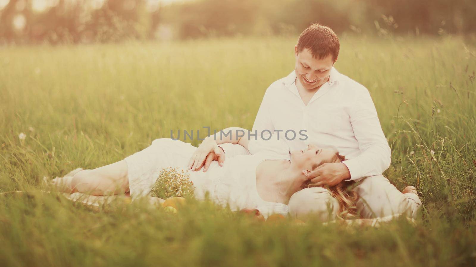 Happy couple - pregnant woman and her husband sit on the grass