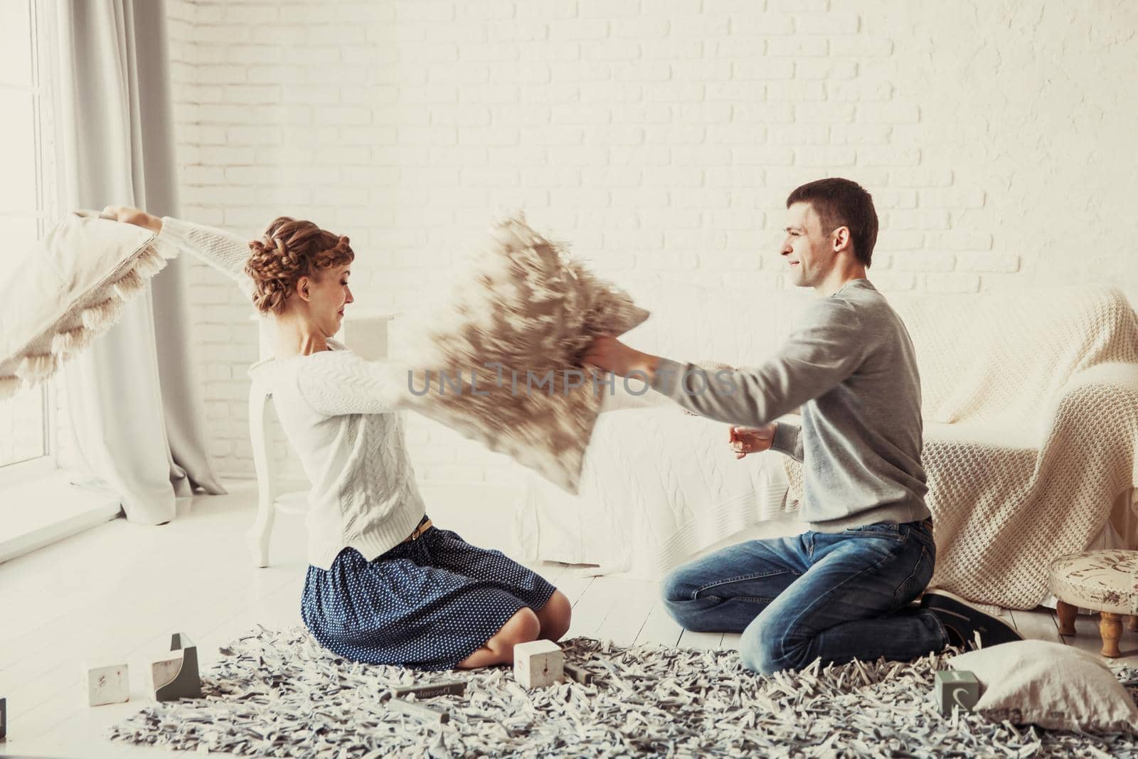 happy husband and wife jokingly holds a pillow fight on the sofa in the living room