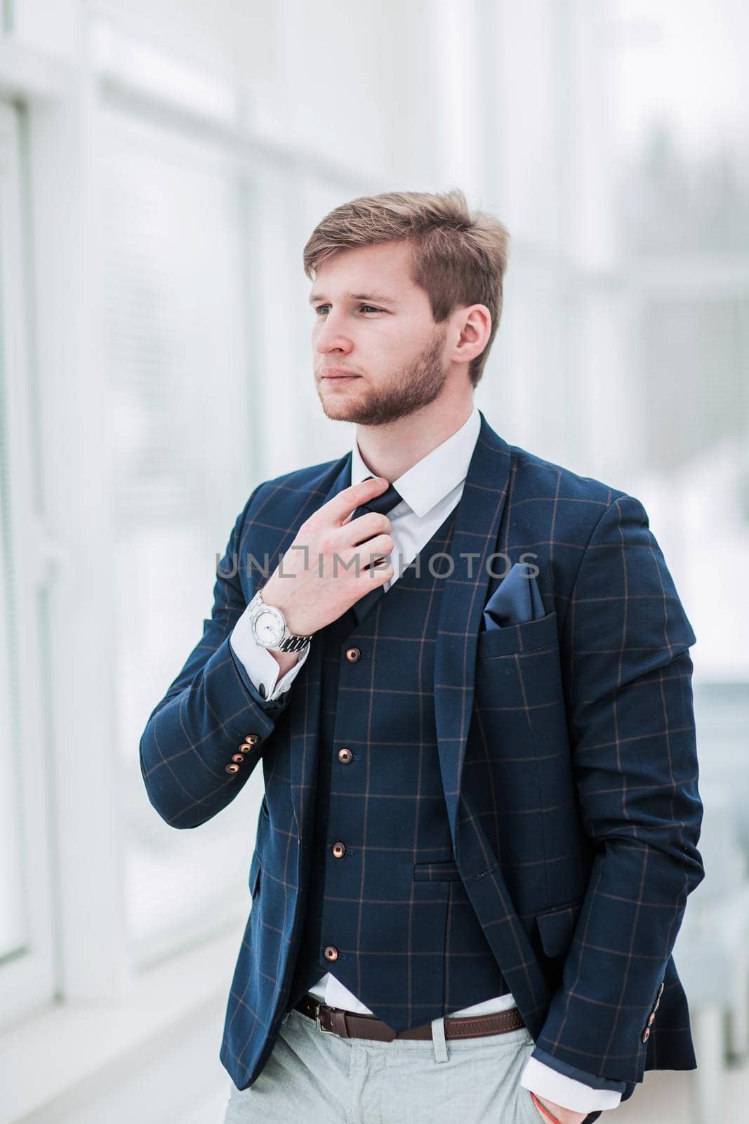 pensive newcomer businessman in a business suit stands near the window and straightens his tie .the photo has a empty space for your text