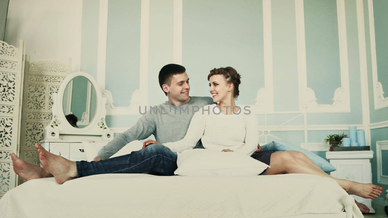 Young happy couple sitting in bed in a spacious bedroom and looking at each other