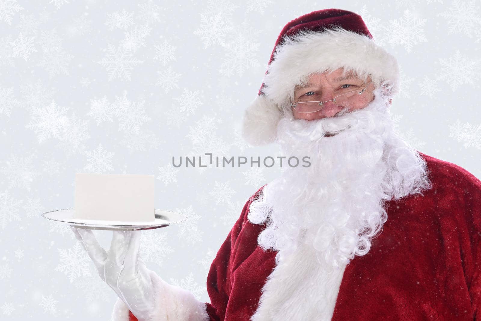 Santa Claus holding a silver platter with a blank note card, over a snow flake background with snow effect. by sCukrov