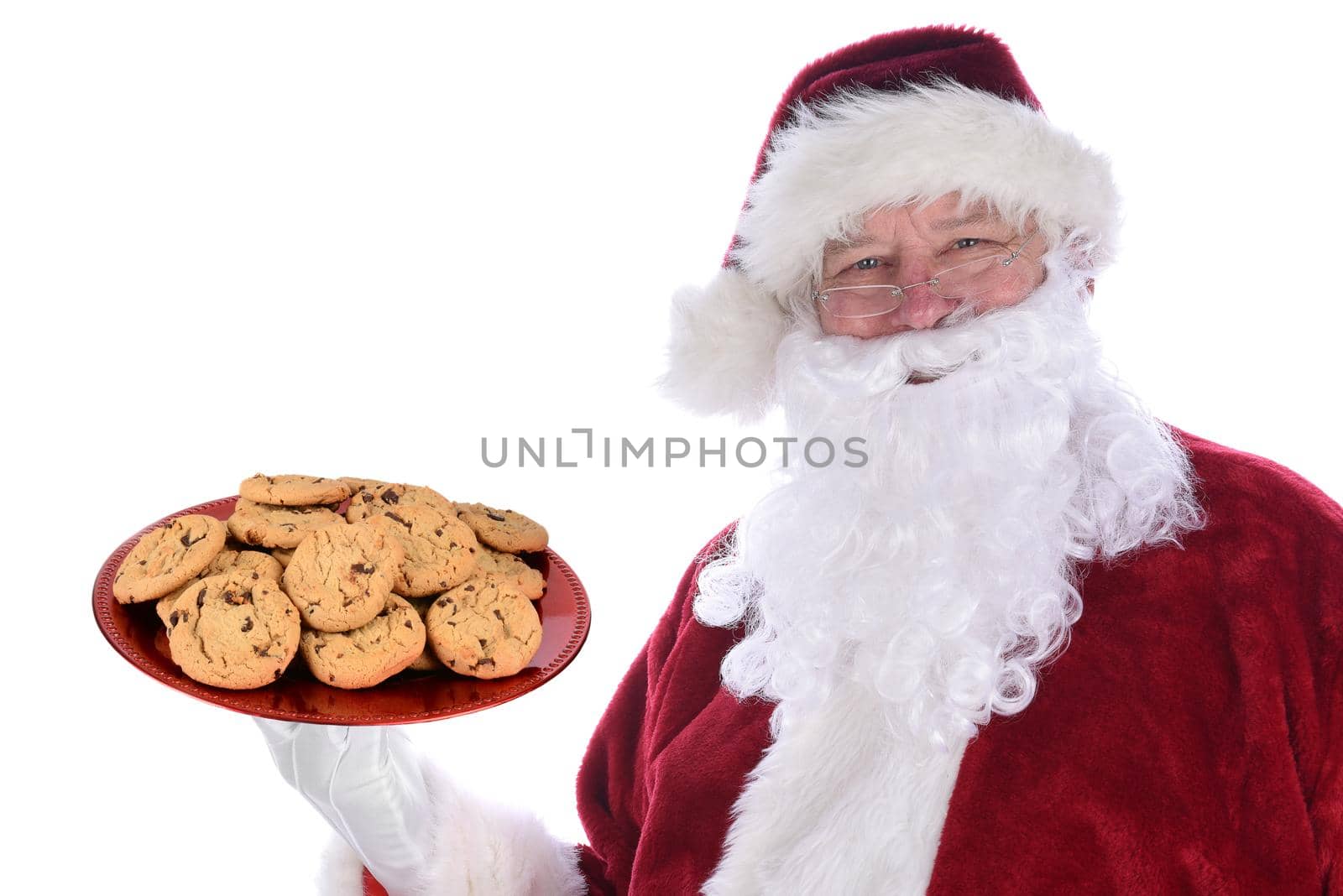 Santa Claus holding a large red platter full of fresh baked chocolate chip cookies, isolated on white.