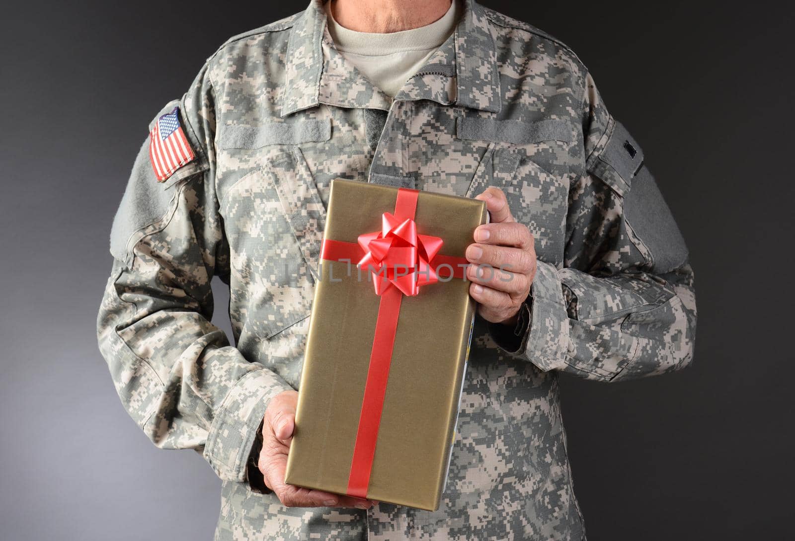 Closeup of a soldier holding a Christmas present. The gift is wrapped in gold paper with red ribbon and bow. Horizontal format. Man is unrecognizable.