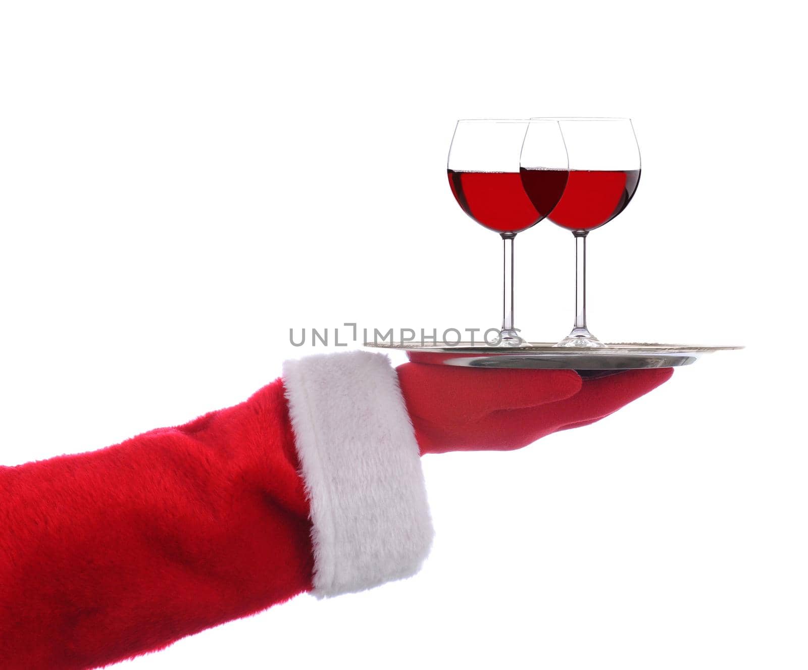 Santa Claus outstretched arm holding a silver serving tray with two glasses of red wine over a white background.