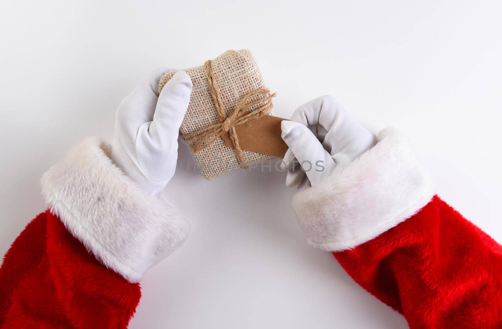 Overhead shot of Santa Claus hands holding a fabric wrapped Christmas Present with a blank gift tag.