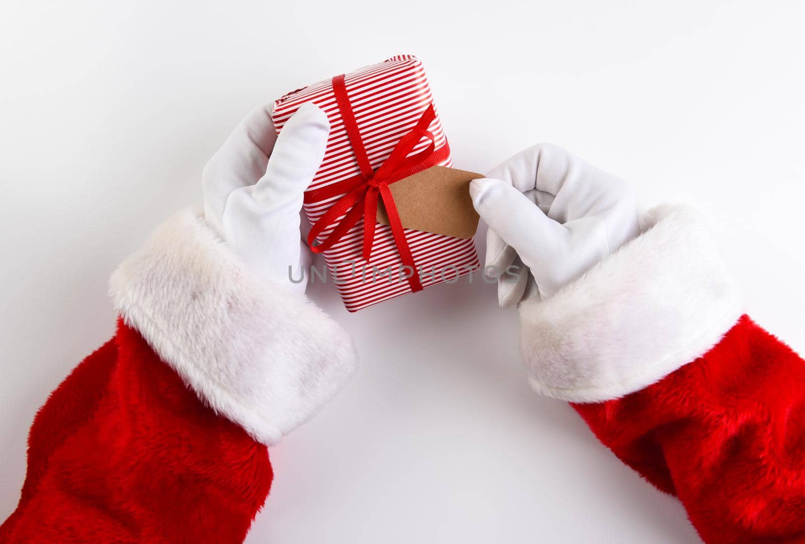 Overhead shot of Santa Claus hands holding a Christmas Present wrpped in red striped paper with a blank gift tag. by sCukrov