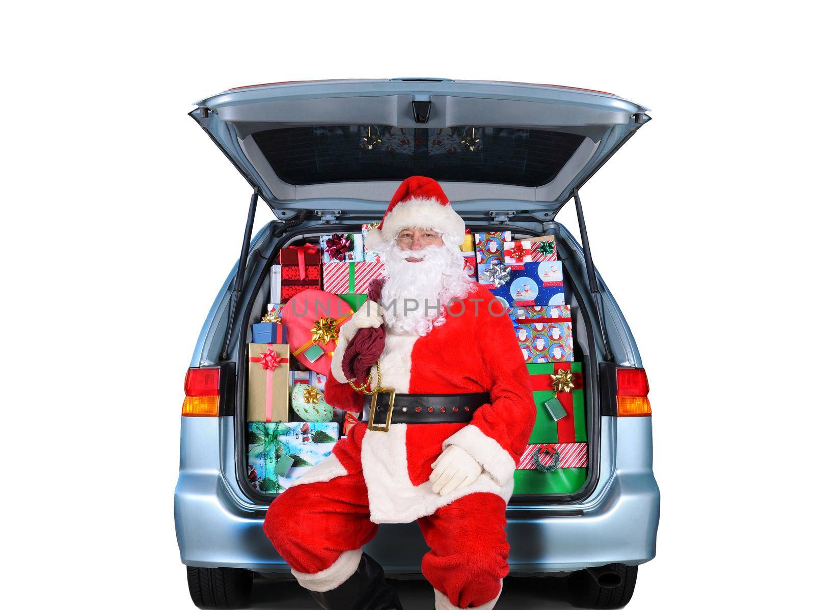 Santa Claus sitting in a Minivan with its rear door open and stuffed full with wrapped Christmas presents. Isolated on white.