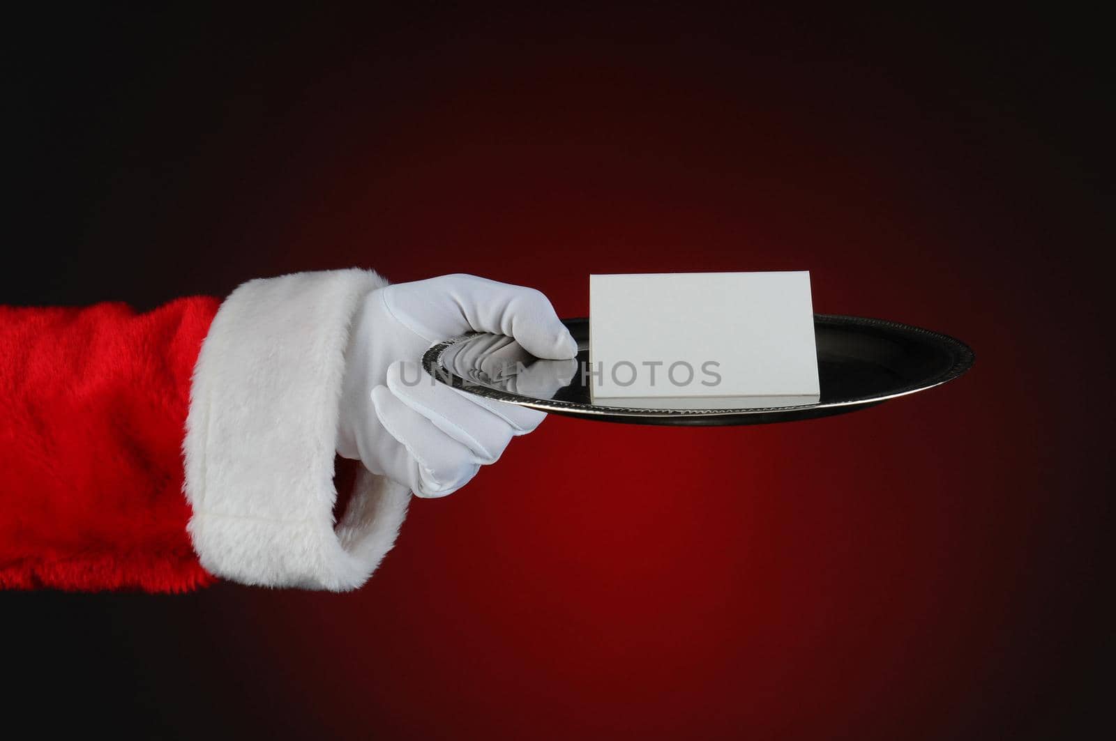 Santa Claus holding a silver serving tray with a blank card. Horizontal format over a light to dark red background.