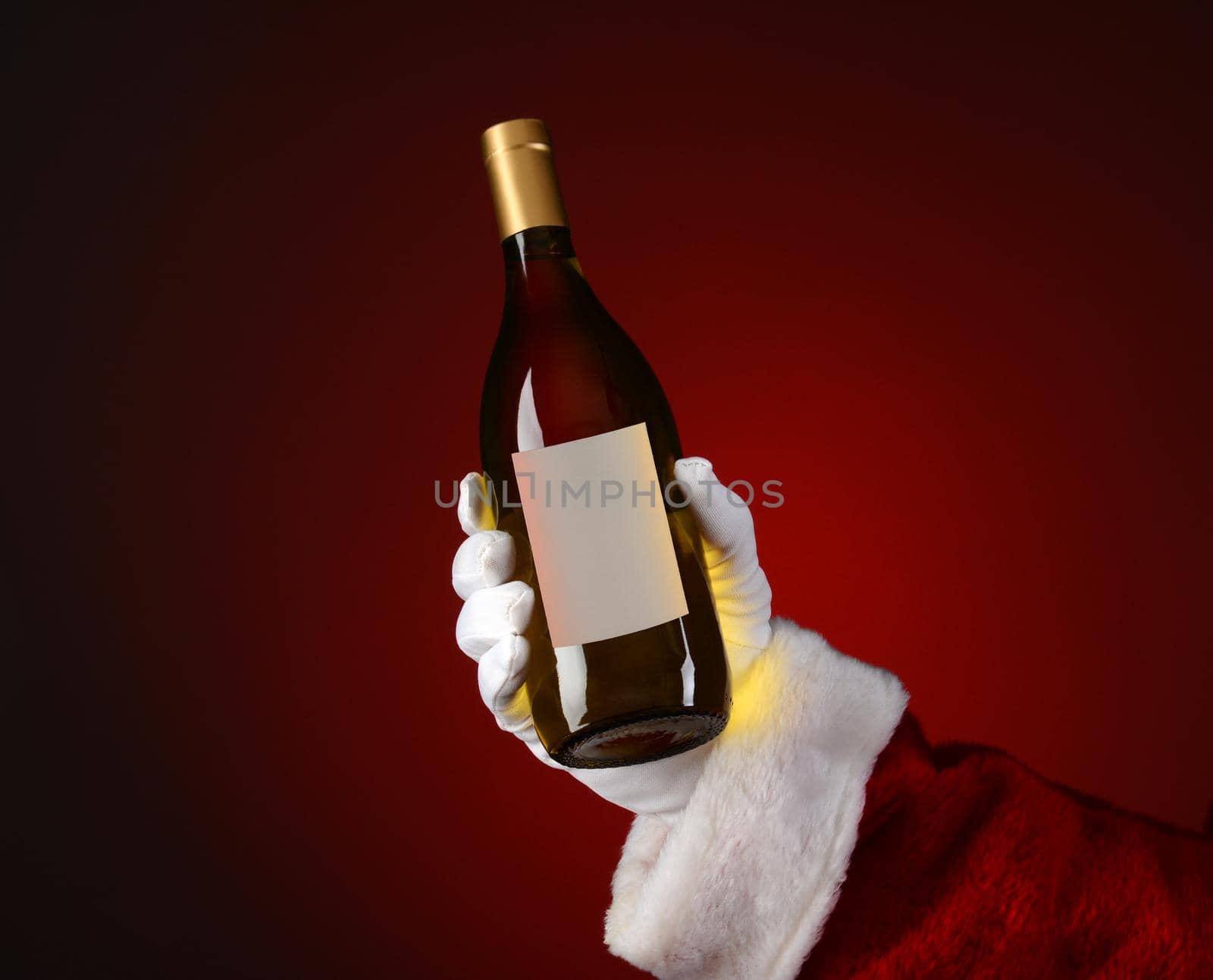 Closeup of Santa Claus holding a bottle of Chardonnay wine in his hand. Hand and arm only over a light to dark red spot background.