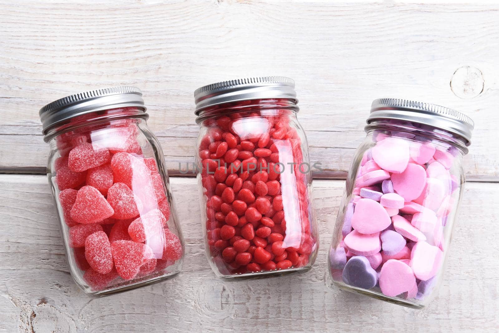 Canning jars laying on their sides filled with candy hearts and for Valentine's Day  on a rustic wood table.