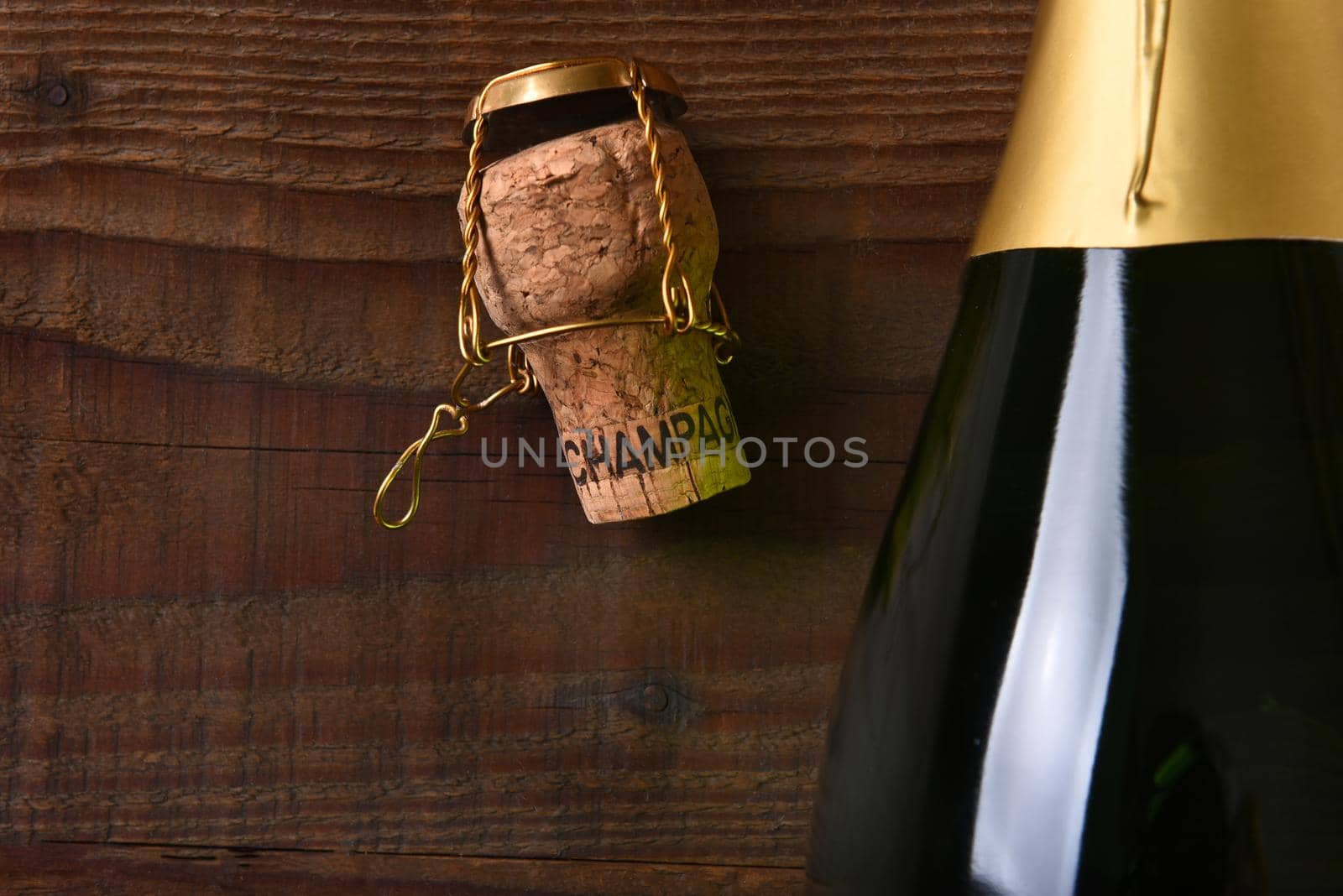 Overhead view of a Champagne bottle next to a cork and cage. Horizontal format on a dark wood background, with copy space.