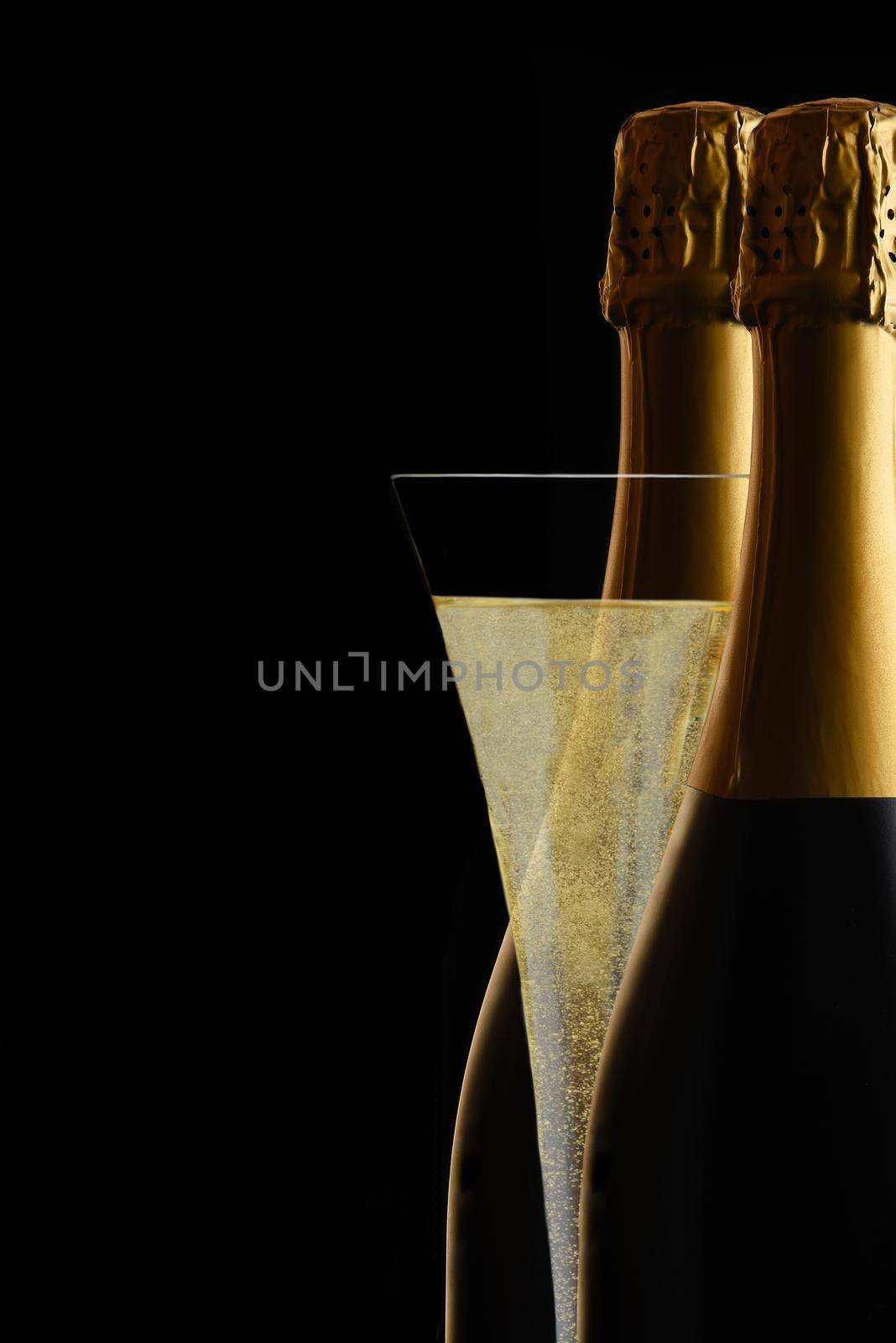 A Champagne Flute between two bottles of Sparkling Wine against a black background..