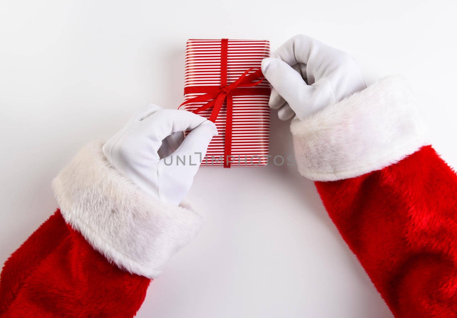 High angle shot of Santa Claus hands tying a ribbon and bow on a res and white striped Christmas Present. by sCukrov