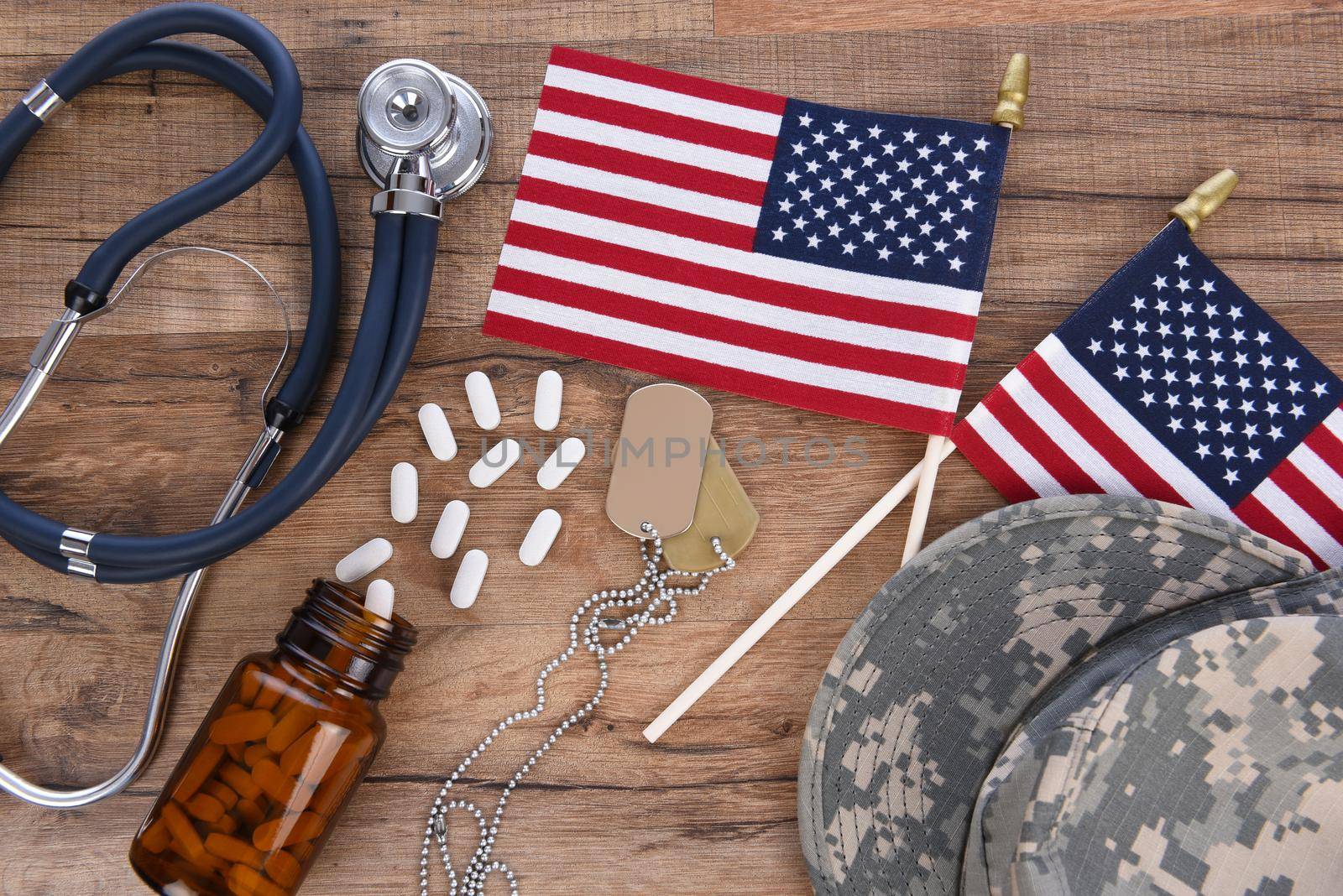Military and Veterans Health Care Concept. Camo hat, dog tags, stethoscope, pills, and American Flags on a wood background.  by sCukrov