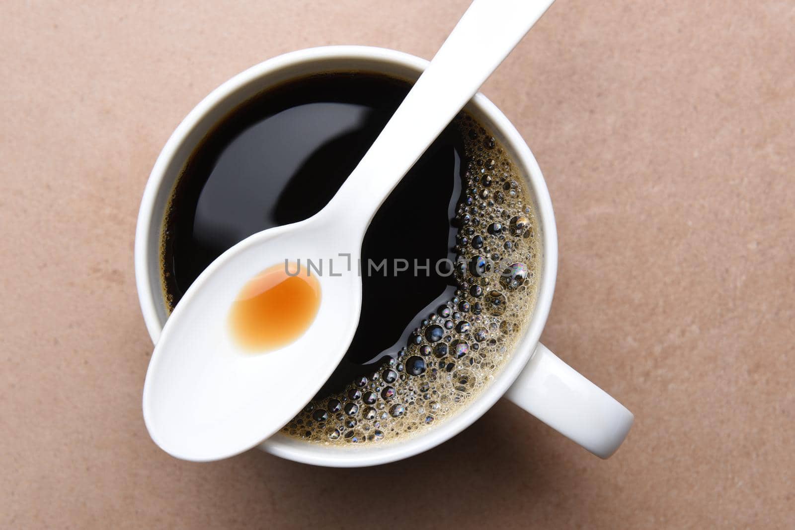 Top view of a plastic spoon laying across the top of a white coffee mug. 