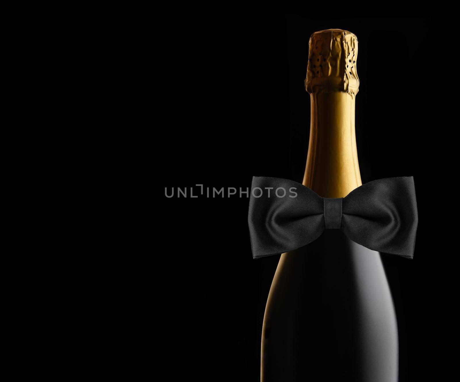 Closeup of an unopened bottle of Champagne against a black background with Black Bow Tie. Ideal for Wedding, Anniversary or New Years Projects, with copy space. 