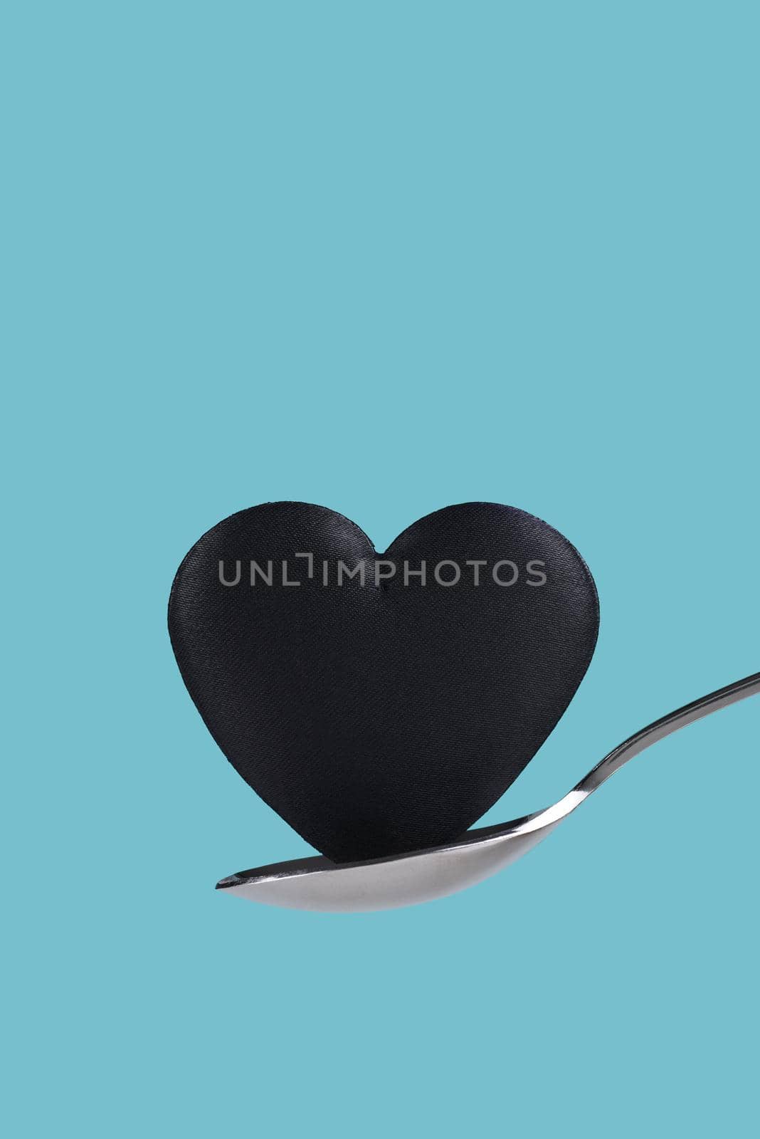 A black heart balanced on a spoon over a teal background.