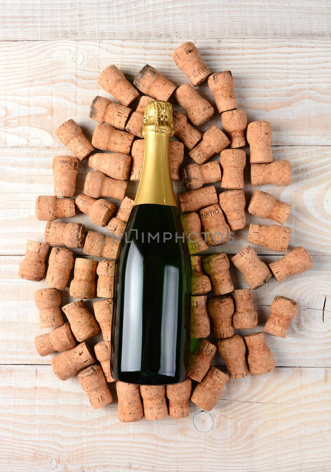 High angle shot of an champagne bottle laying on its side and surrounded by old used corks. Horizontal format on a rustic white wood background.