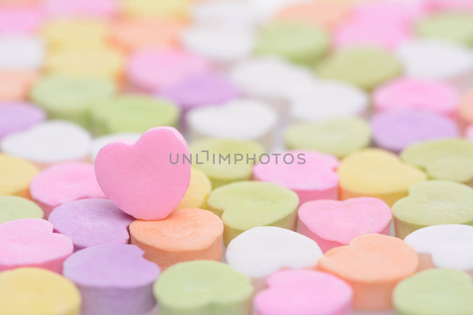 Closeup of a pink candy heart for Valentines Day standing out in a field of out of focus similar candies. Heart is set to one side leaving room for your copy. The candies are blank.
