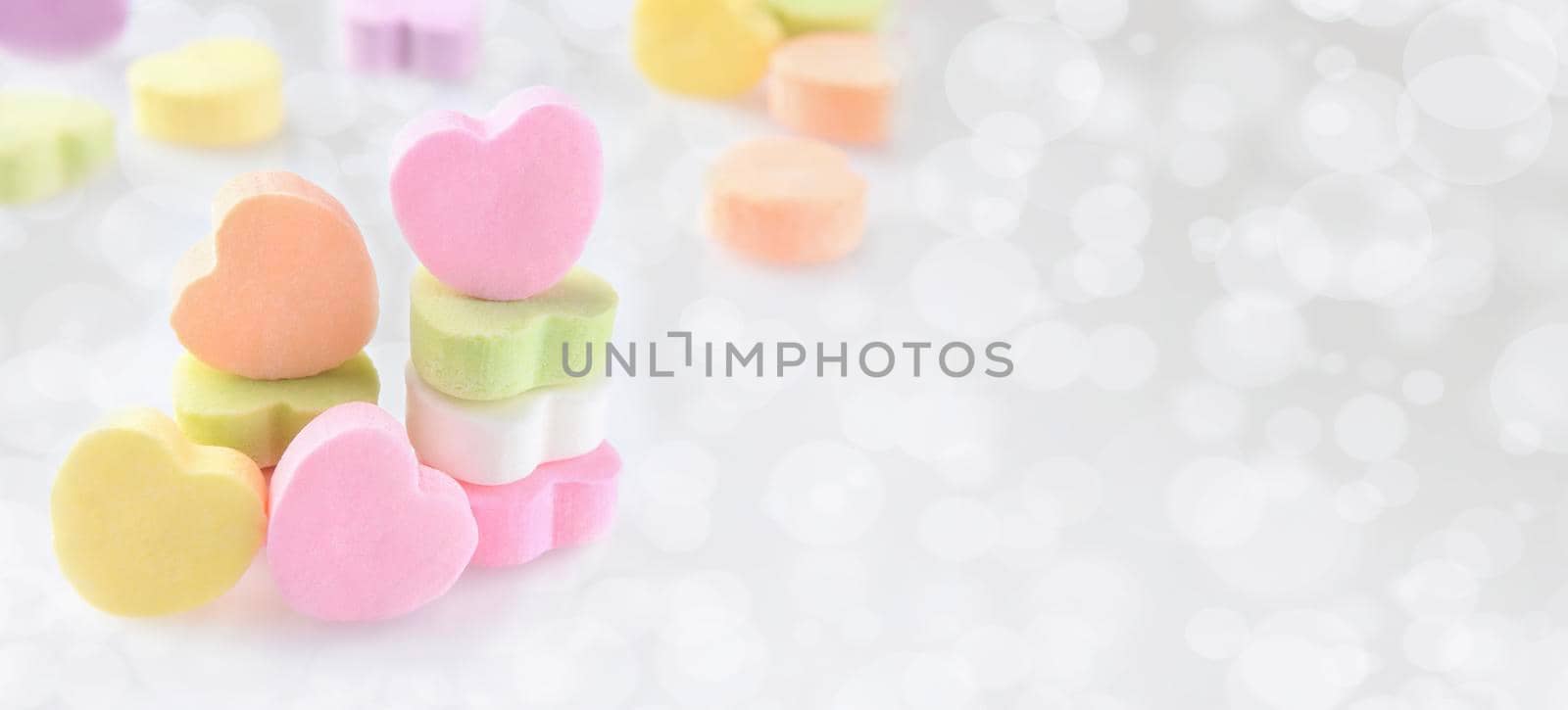Valentines Day Banner: Pastel Candy hearts on a silver bokeh background with copy space.