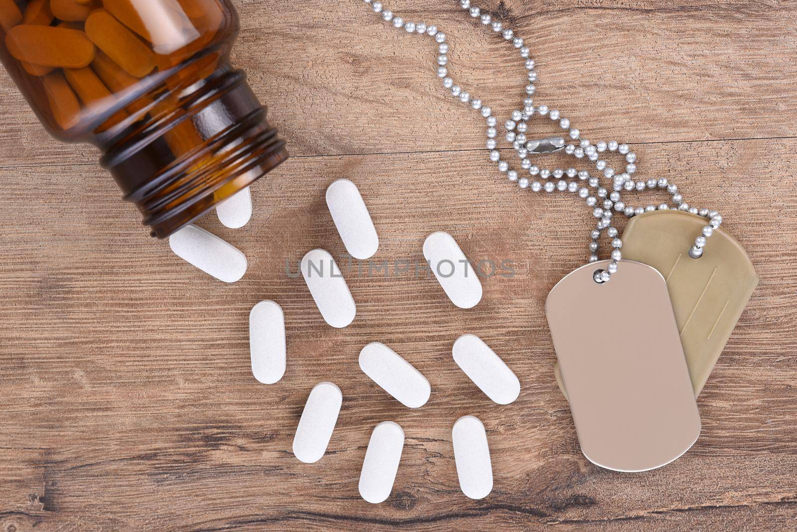 Military and Veterans Health Care Concept. Dog tags and pill bottle with tablets spilling onto the wood table background. by sCukrov