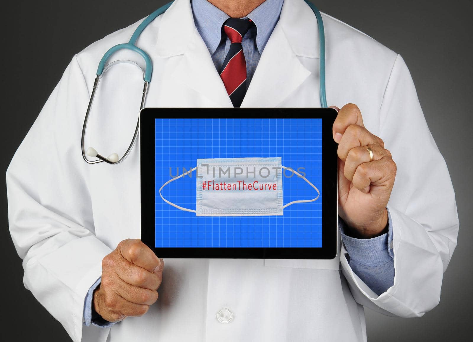 Closeup of a doctor holding a tablet computer with a Surgical mask and Flatten the Curve by sCukrov