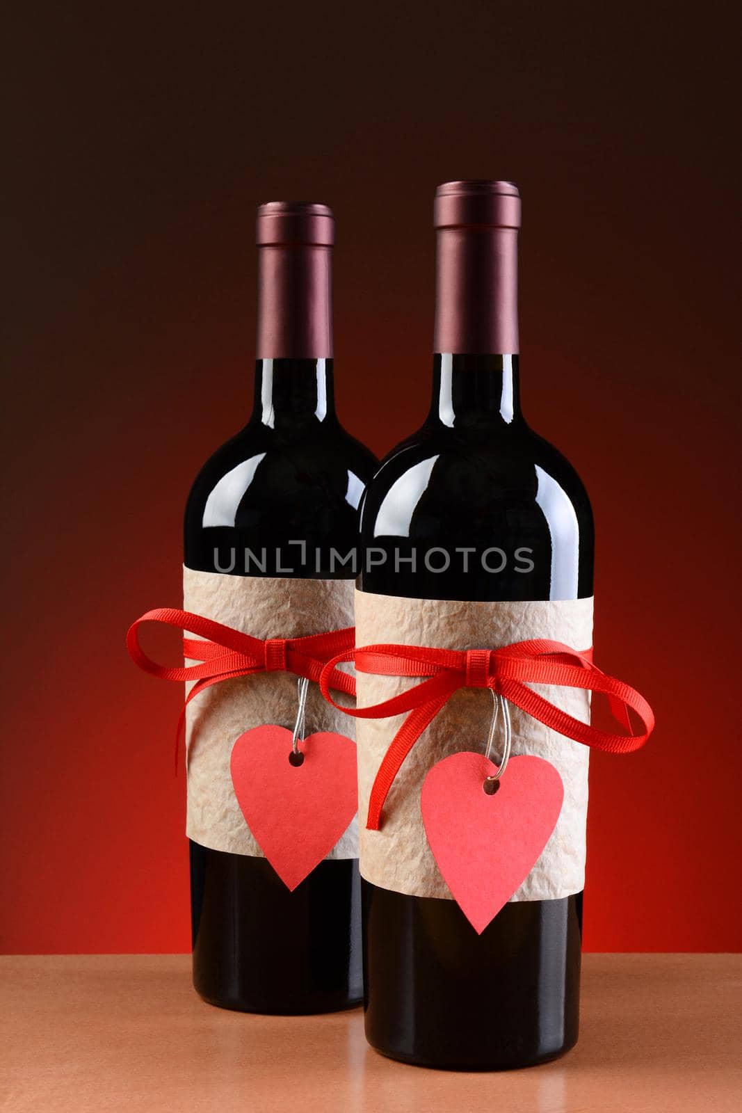 Closeup of a wine bottles decorated for Valentines Day. Both bottles have a red ribbon and heart shaped tag and a blank label. Vertical Format.