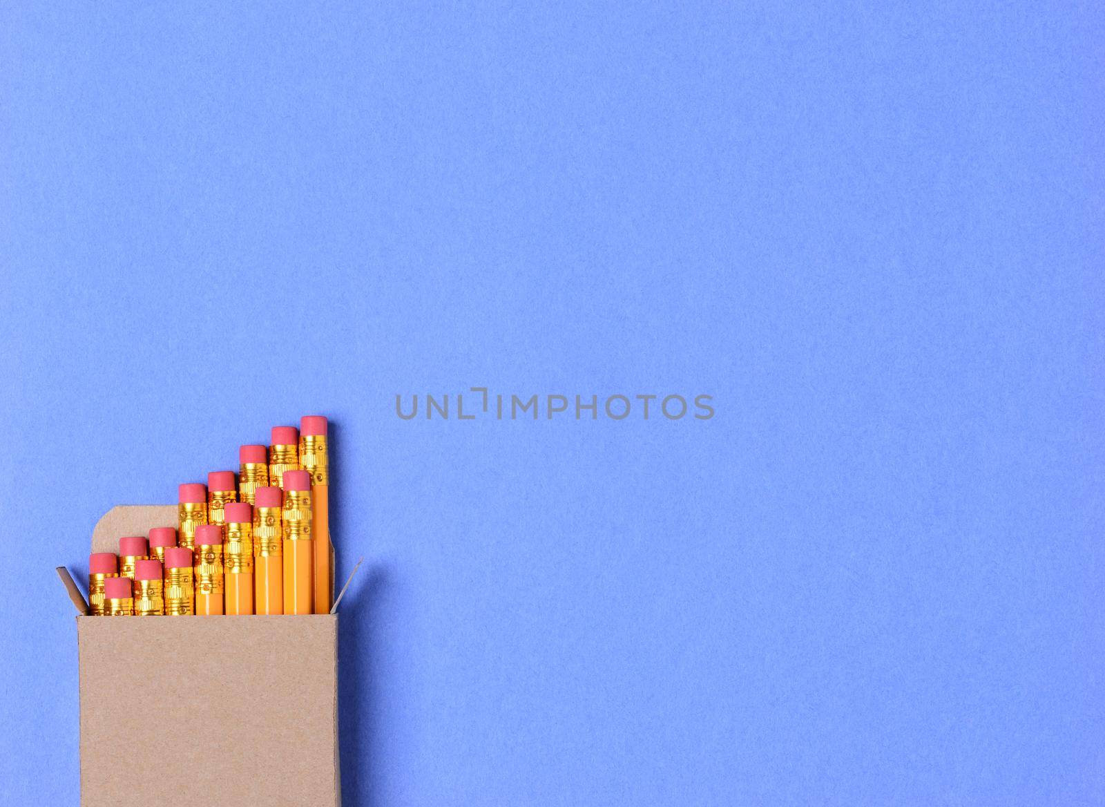 High angle shot of a box of new yellow pencils on a blue construction paper background. Horizontal format with copy space. Perfect for Back to School concepts.