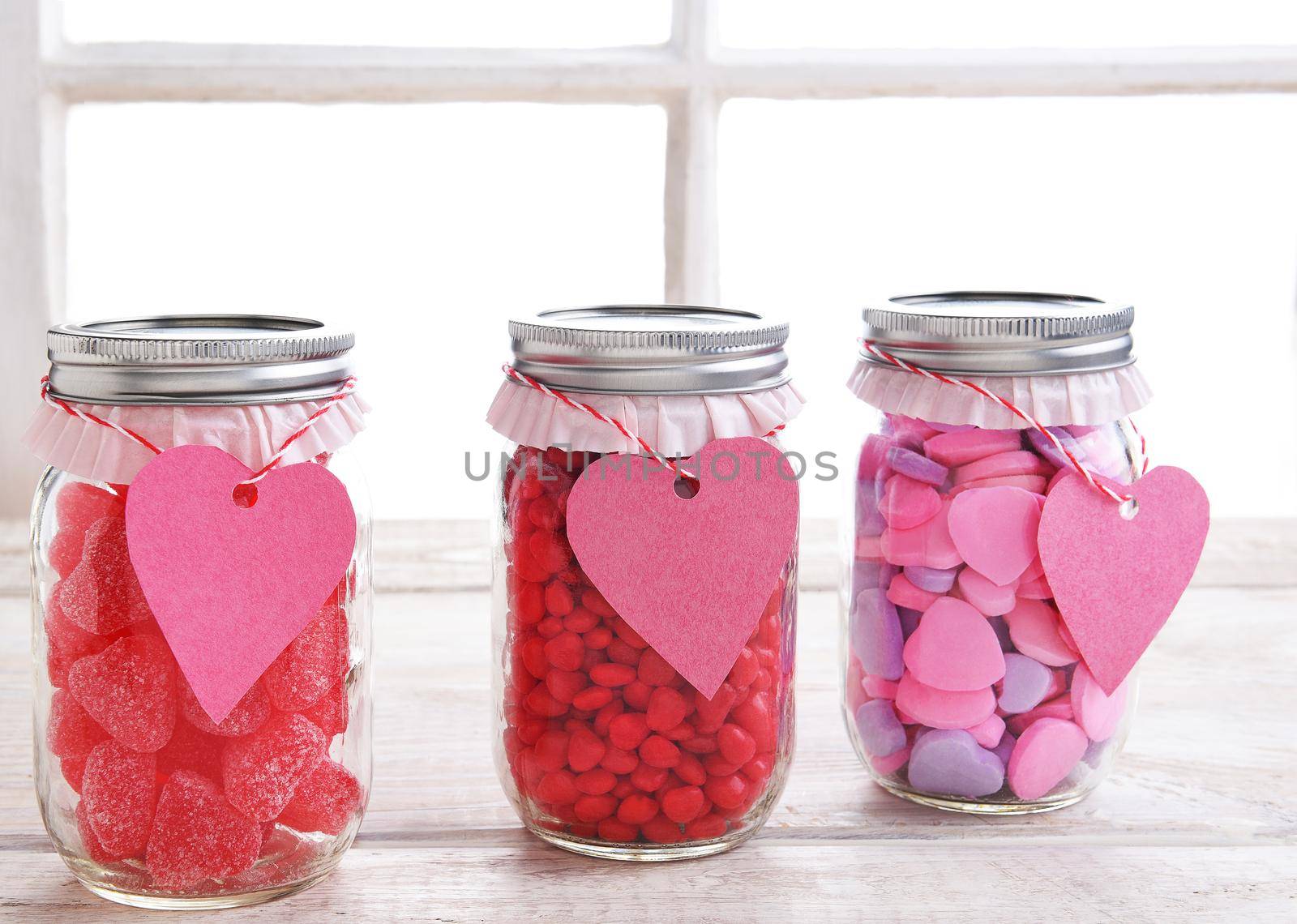 Canning jars filled with candy hearts and decorated for Valentine's Day with a heart shaped gift tag. 